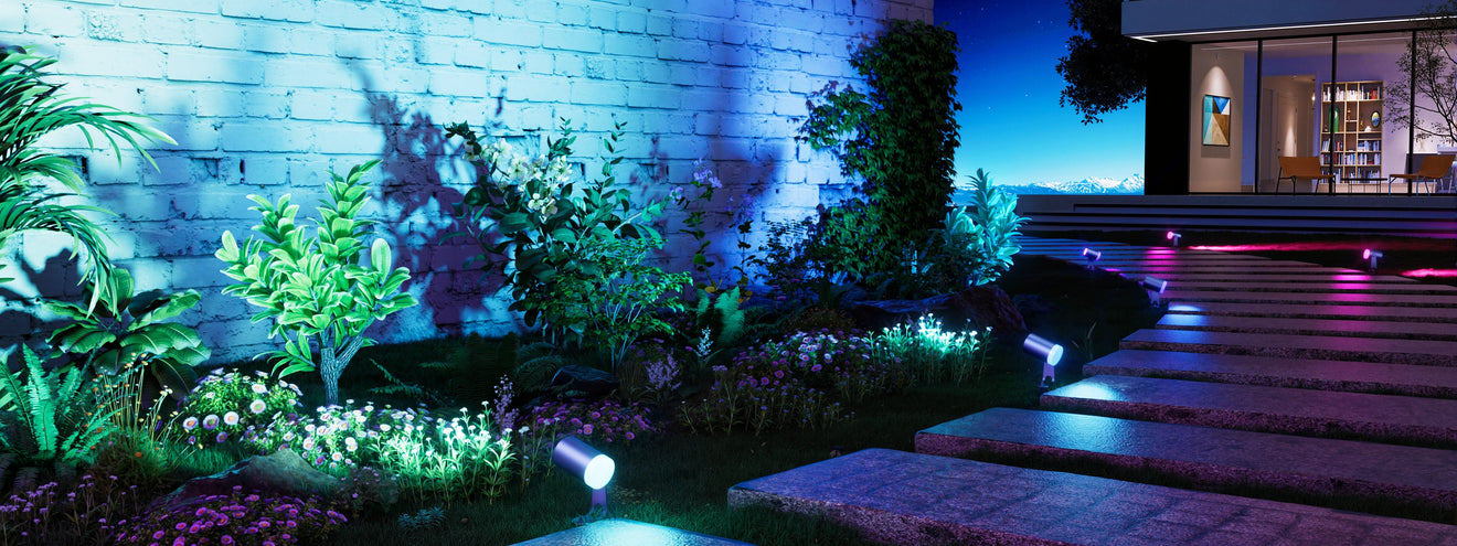 Smart outdoor spotlights illuminating garden wall, plants, and pathway with colorful RGB landscape lighting at night