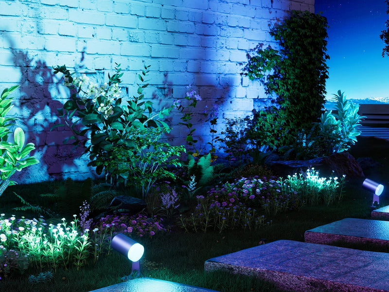 Smart outdoor spotlights illuminating garden wall, plants, and pathway with colorful RGB landscape lighting at night