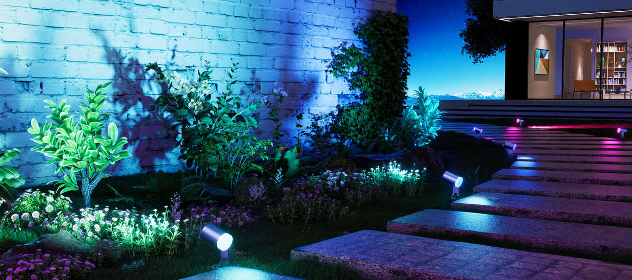 Smart outdoor spotlights illuminating garden wall, plants, and pathway with colorful RGB landscape lighting at night